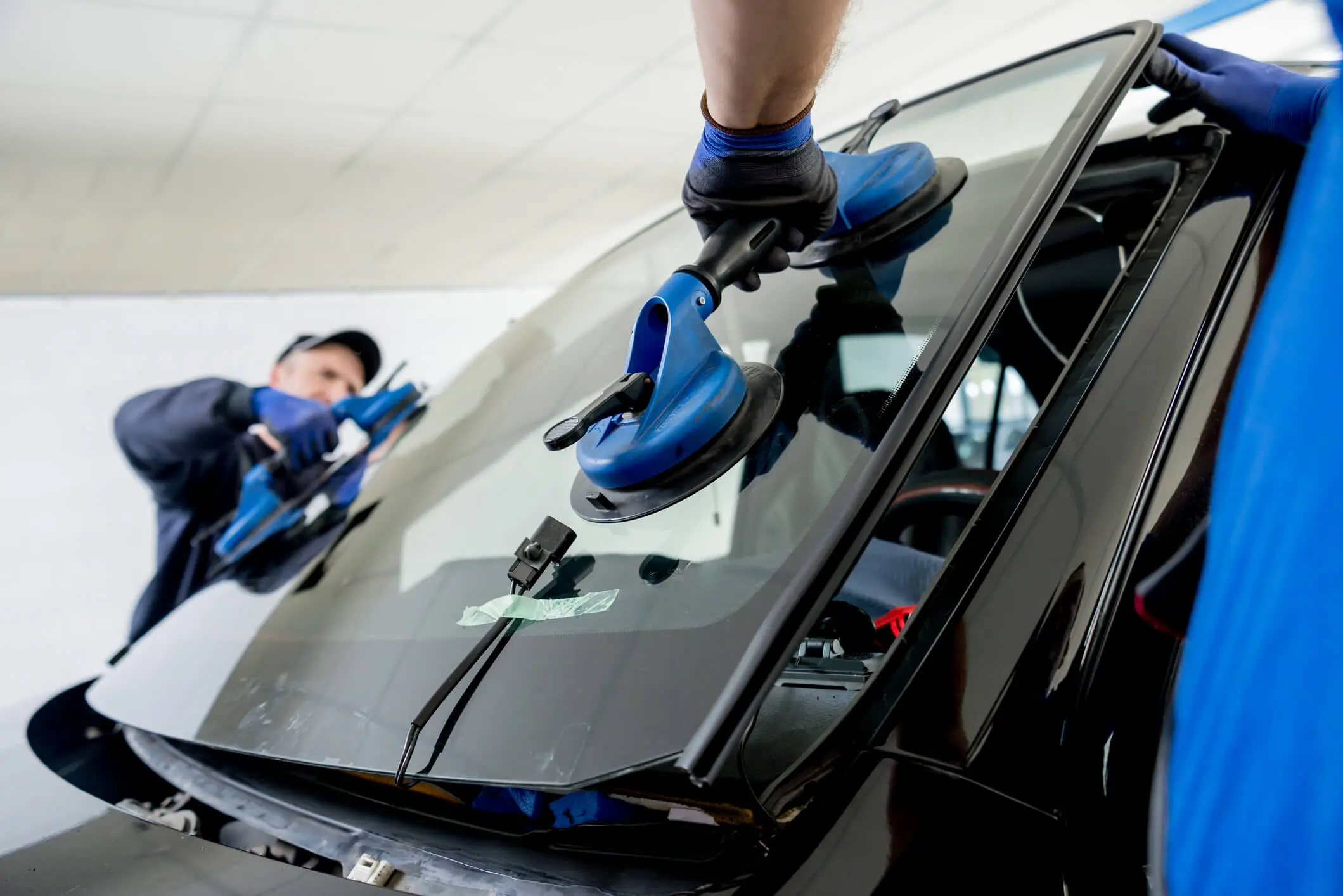Automobile special workers replacing windscreen of a car in auto service. Automobile special workers replacing windscreen or windshield of a car in auto service station garage. Background