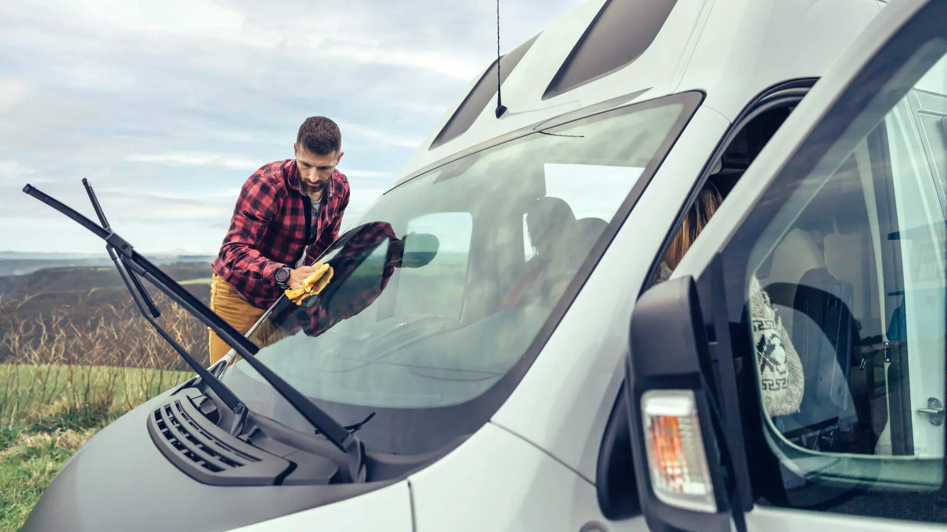 Man cleaning camper van windshield outdoor. Young men cleaning camper van windshield with cloth outdoor