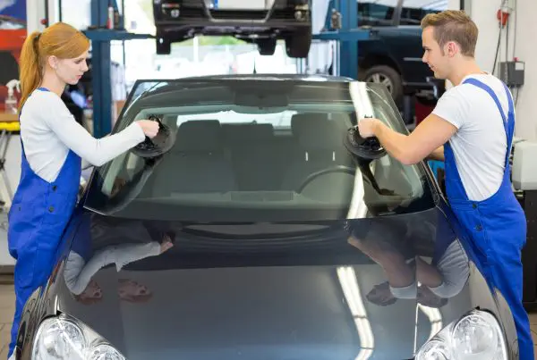 Glaziers replace windshield or windscreen on car after stone-chipping. Mechanics or glaziers install windshield or windscreen for replacement in garage