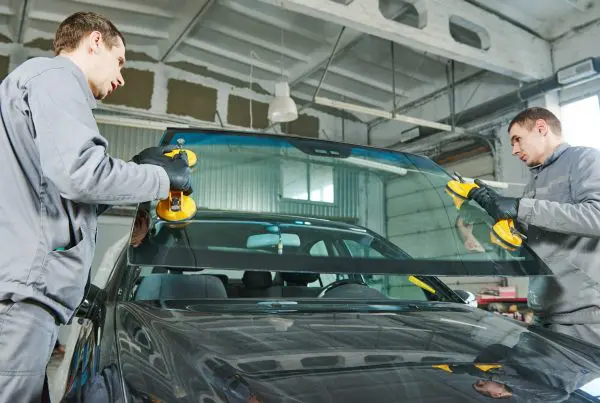 Automobile windshield or windscreen replacement. Glazier repairman mechanic worker replaces windshield or windscreen on a car in automobile workshop garage