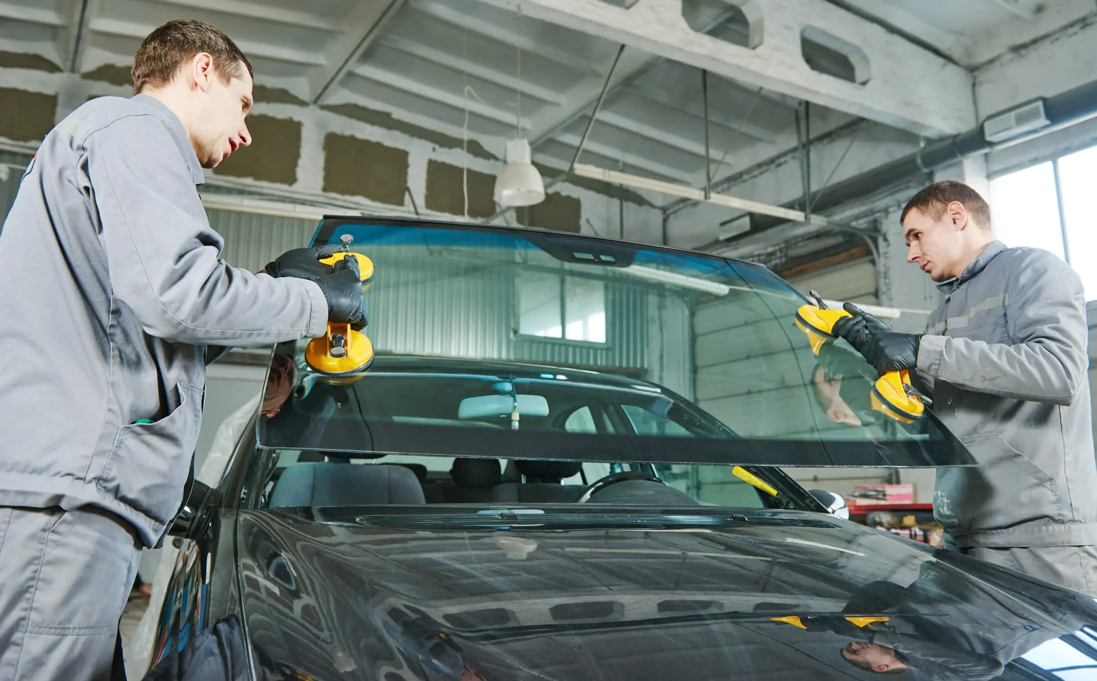 Automobile windshield or windscreen replacement. Glazier repairman mechanic worker replaces windshield or windscreen on a car in automobile workshop garage
